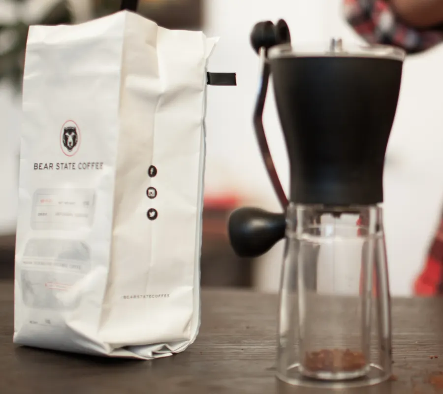 A hand grinder alongside a bag of coffee and a brewer